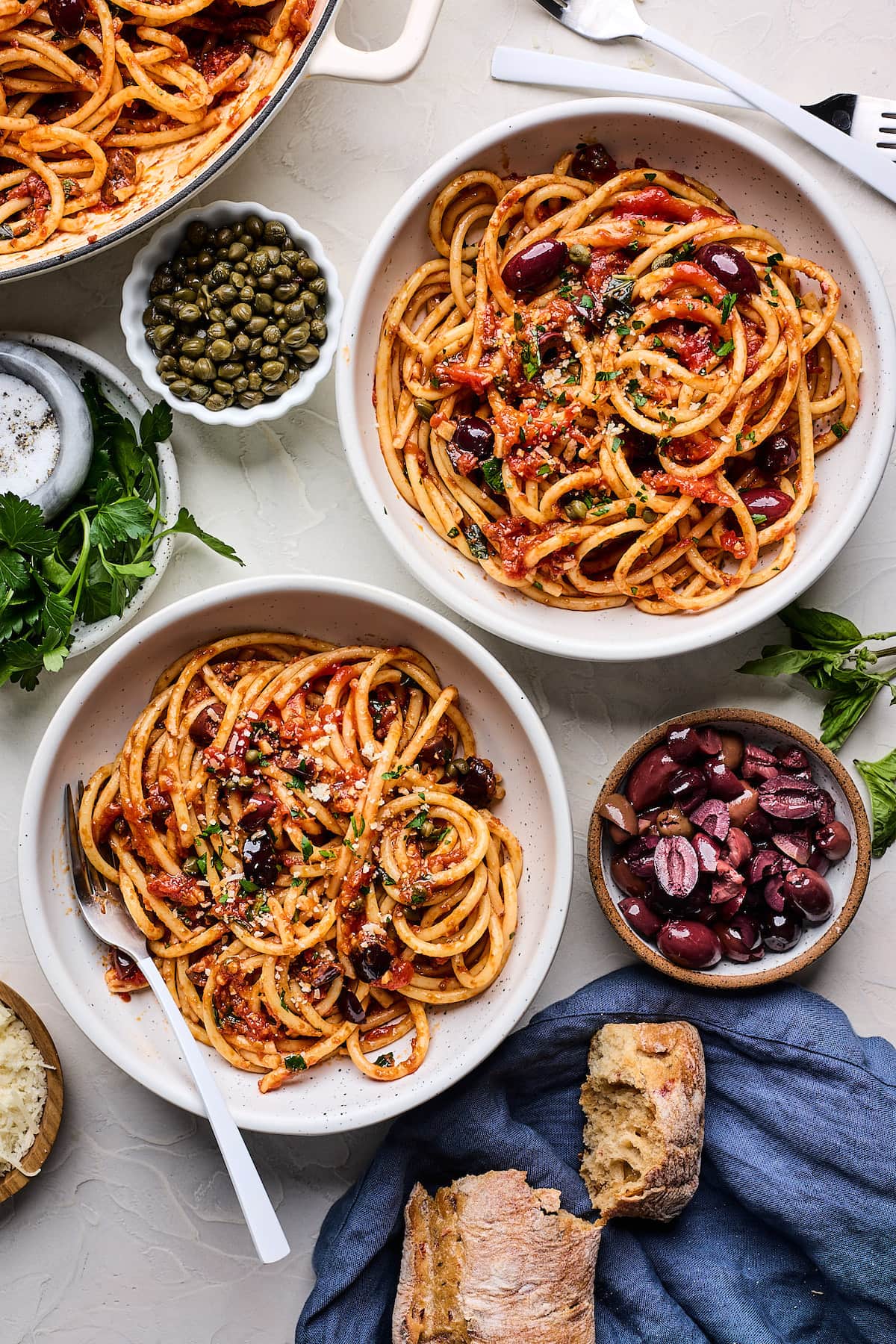 pasta puttanesca in bowls with capers, olives, herbs, and parmesan cheese.