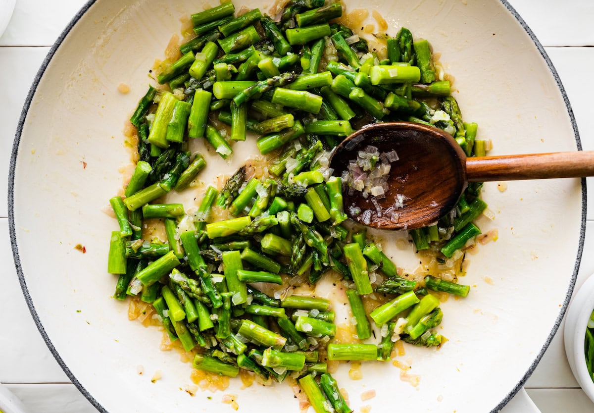 asparagus and shallot cooking in skillet with wooden spoon.