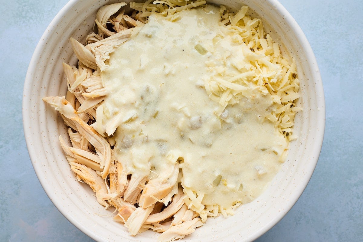 shredded chicken, white chicken enchilada sauce, and cheese in mixing bowl.