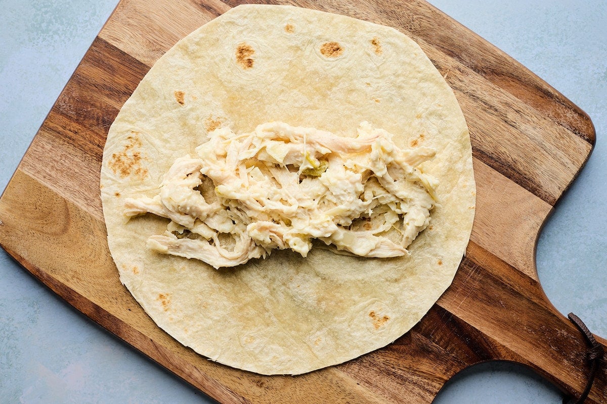 flour tortilla with white chicken enchilada filling on wood board.