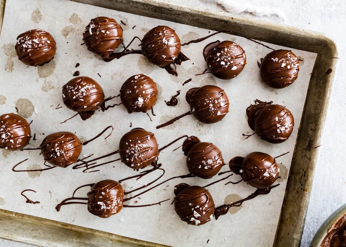 brownie protein balls dipped in chocolate with flaky sea salt on baking sheet with parchment paper.