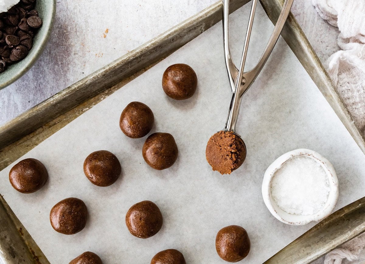 brownie protein balls being scooped onto baking sheet with parchment paper.