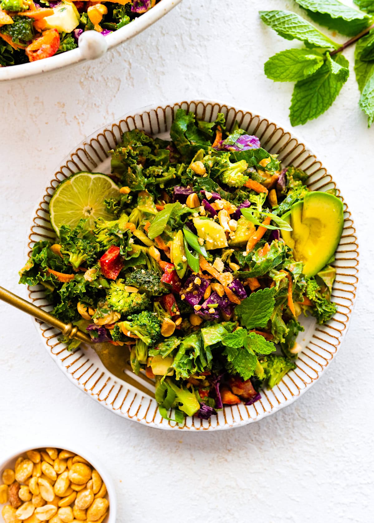 chopped kale broccoli salad with peanut dressing in bowl with lime, avocado, and a fork.