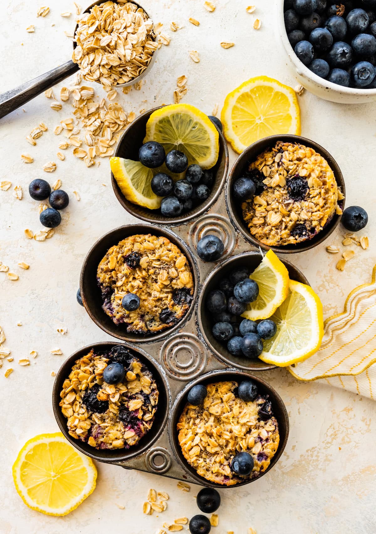 lemon blueberry baked oatmeal cups in muffin pan with fresh blueberries and lemon wedges.