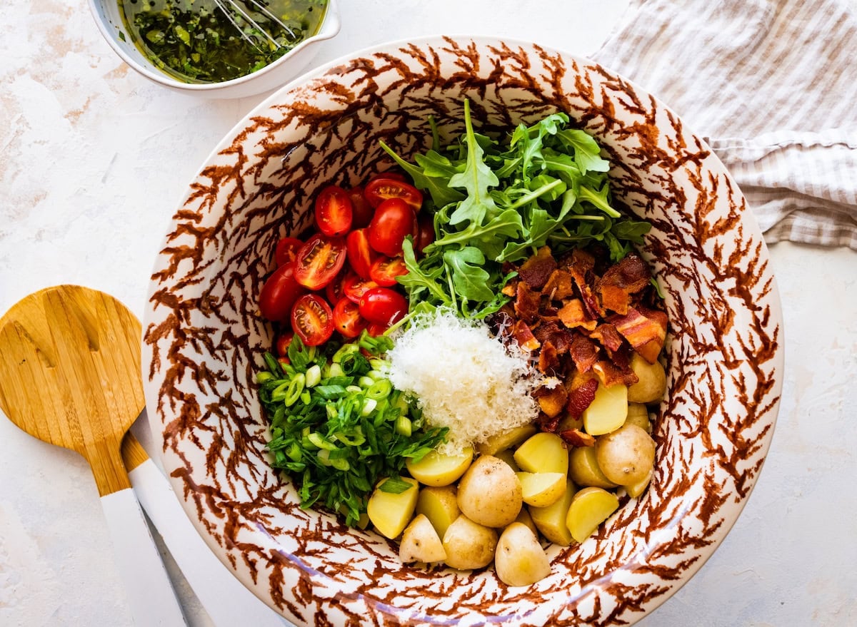 potatoes, bacon, arugula, tomatoes, green onion, herbs, and Parmesan cheese in mixing bowl to make no mayo potato salad.