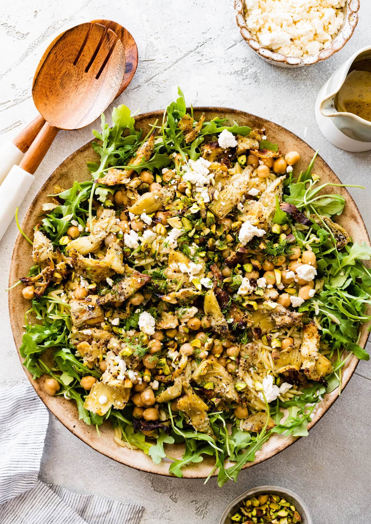 roasted artichoke chickpea orzo salad with arugula, feta cheese, and pistachios in bowl.