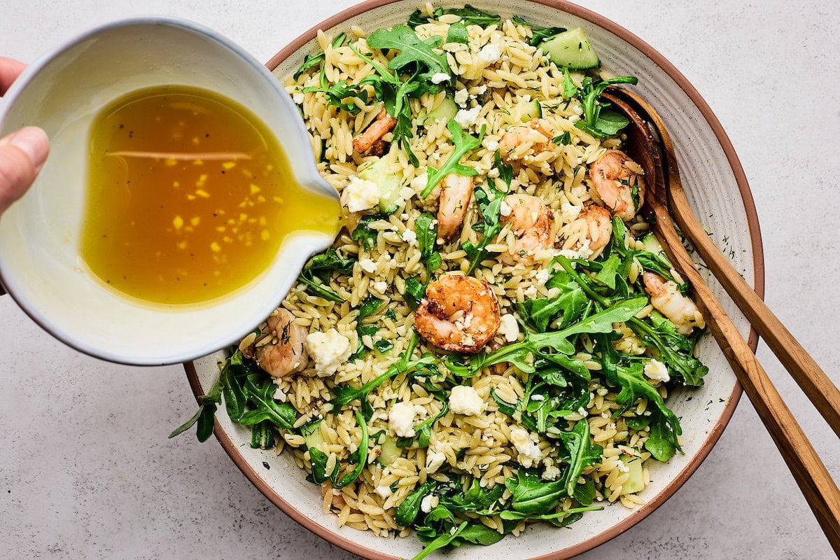 dressing being poured over shrimp orzo salad.
