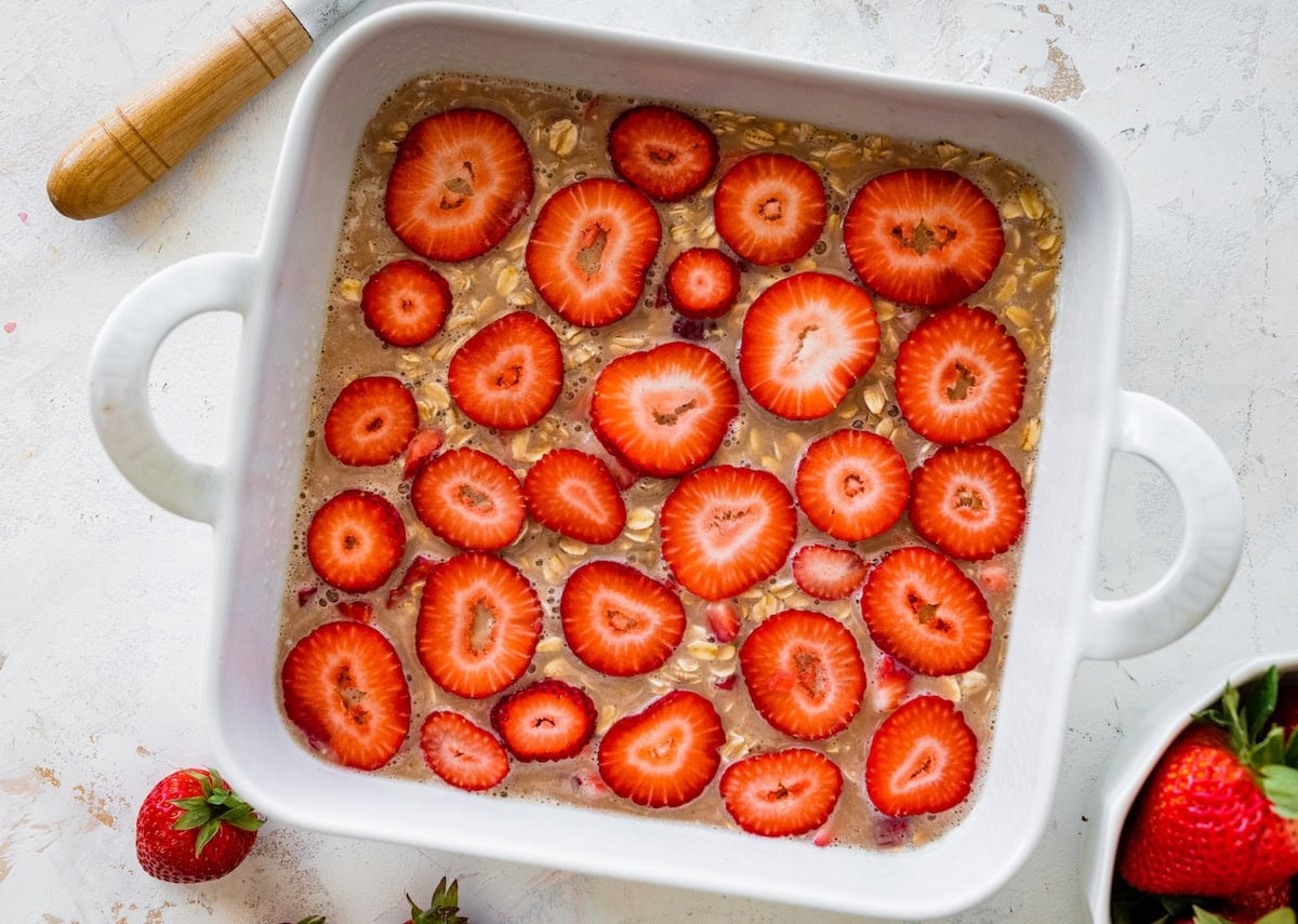 strawberry baked oatmeal mixture in baking dish with fresh strawberry slices on type.