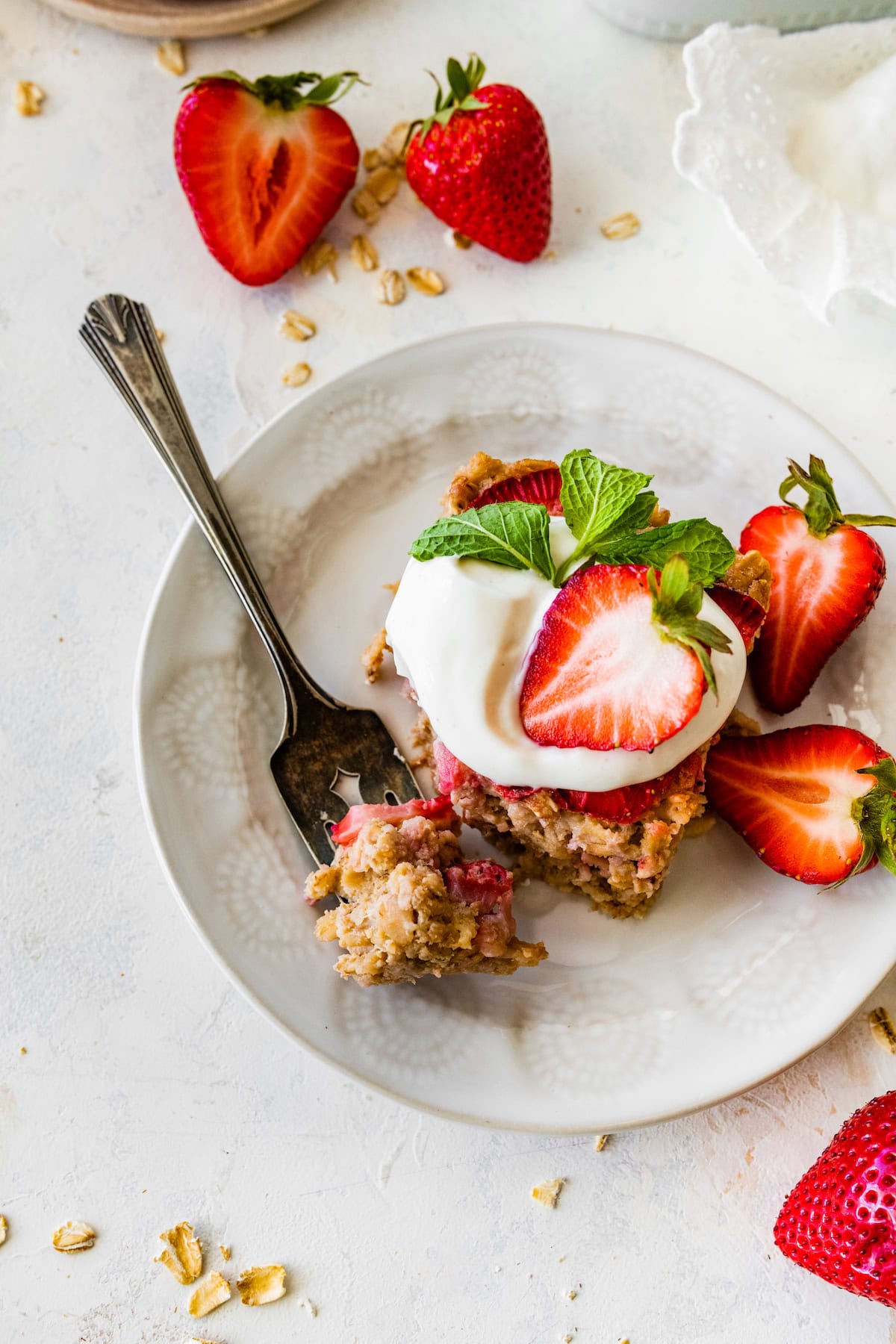 piece of strawberry baked oatmeal with yogurt and fresh strawberries on plate with fork.