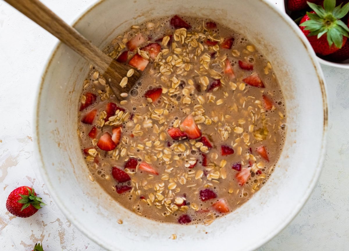 strawberry baked oatmeal mixture in mixing bowl with wooden spoon.