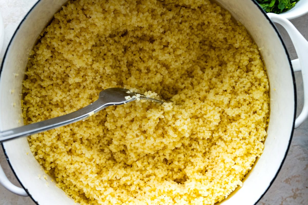 couscous being fluffed with a fork in big white pot.