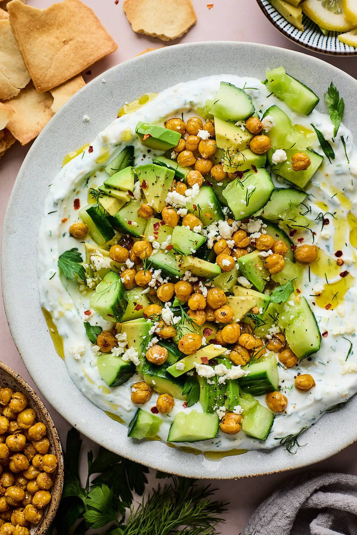 smashed cucumber, avocado, crispy chickpea salad with creamy yogurt feta spread on plate.
