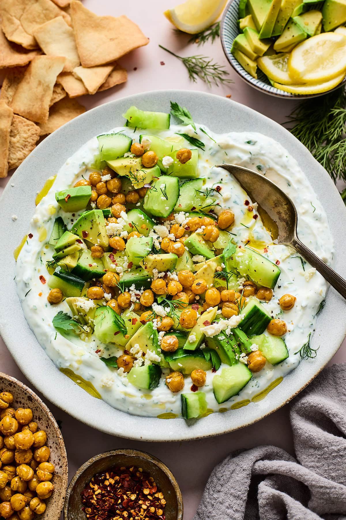 smashed cucumber, avocado, crispy chickpea salad with creamy yogurt feta spread on plate with spoon.