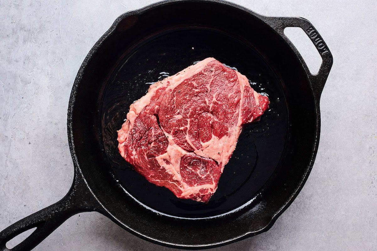 steak cooking in cast iron skillet.