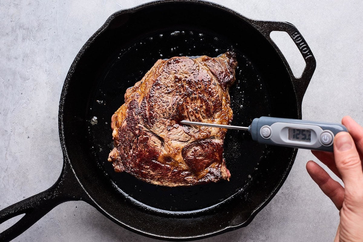 taking temperature of steak in cast iron skillet to make a steak sandwich.