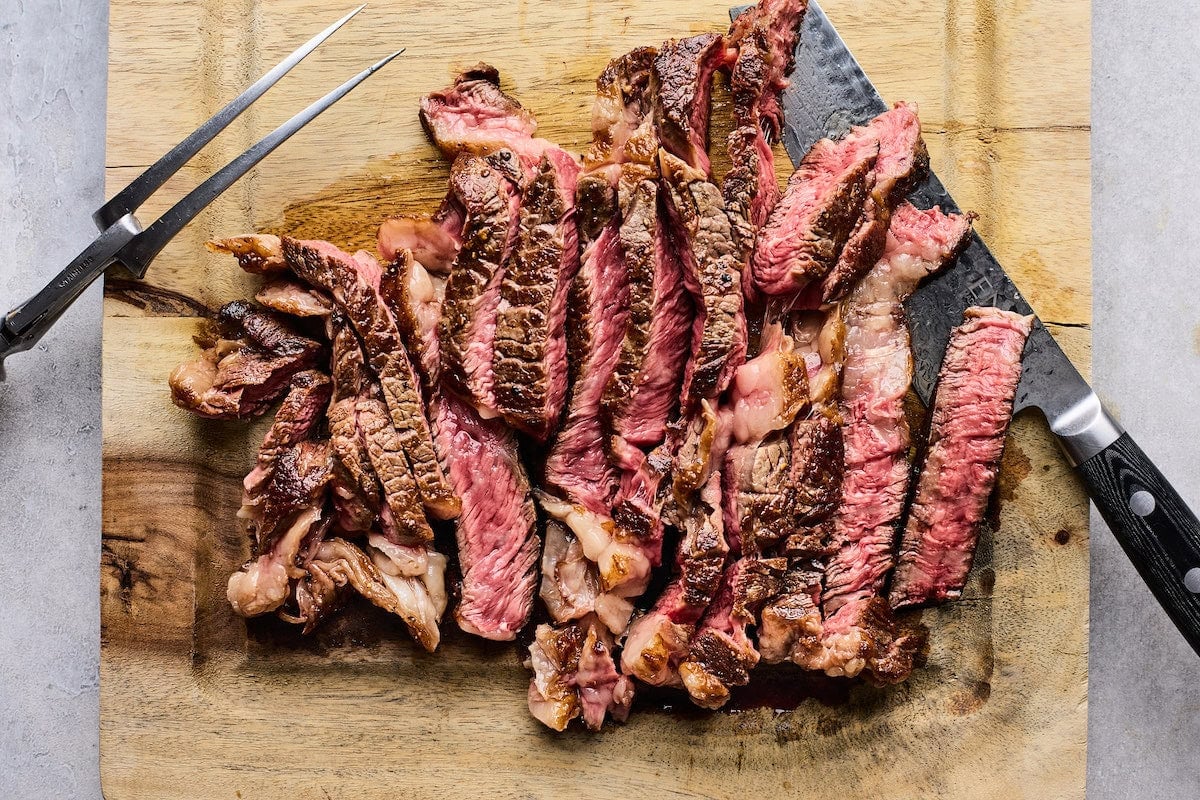 thinly sliced steak on cutting board to make steak sandwich.