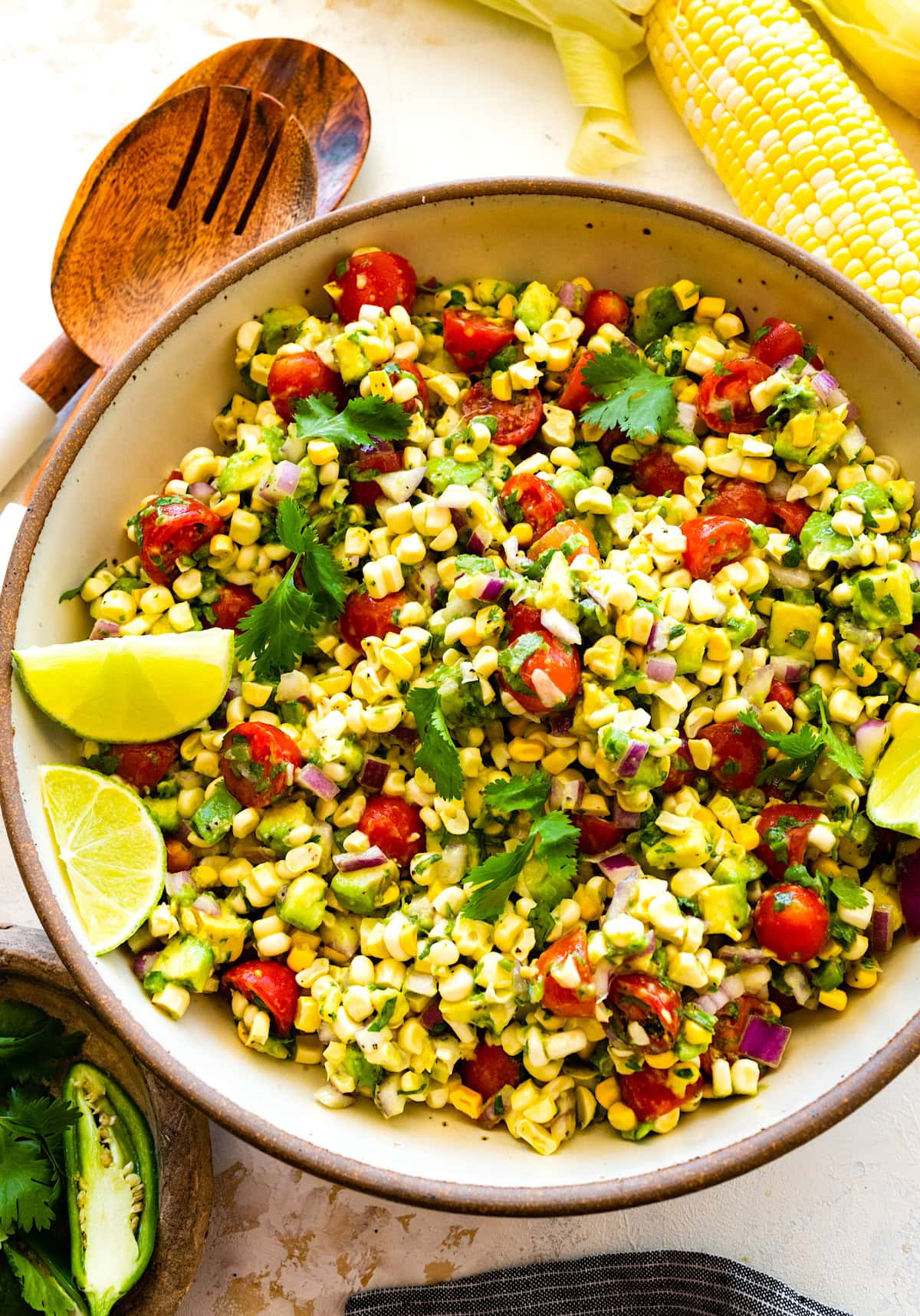 avocado corn salad in bowl with lime wedges.