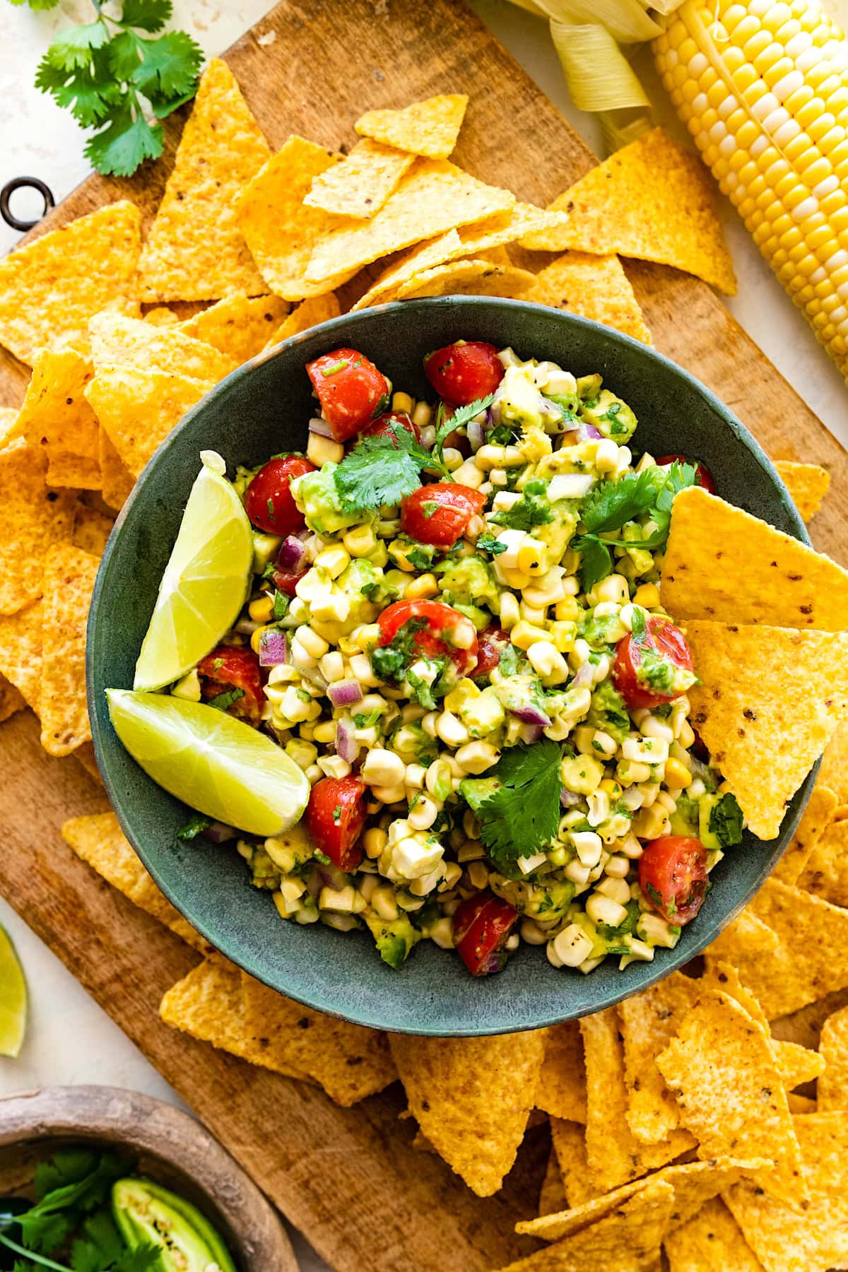 avocado corn salad in bowl with lime wedges and tortilla chips.