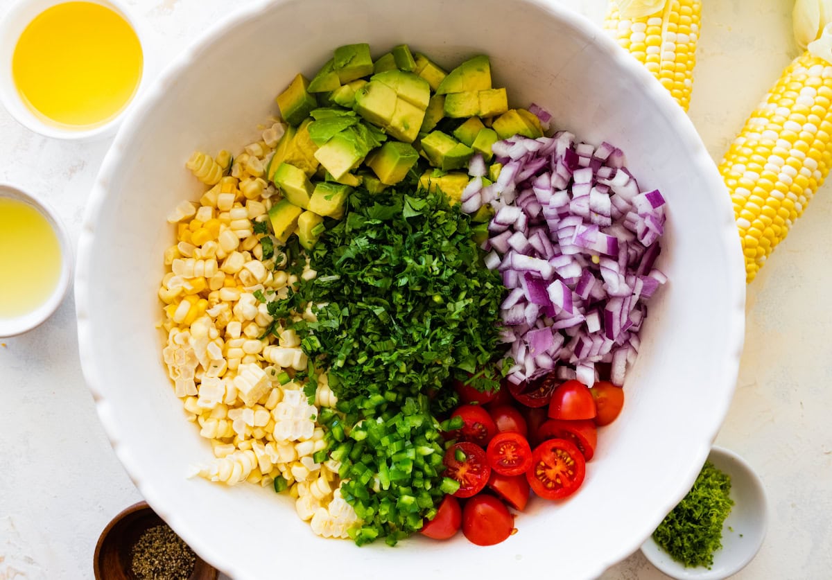 avocado, red onion, tomatoes, jalapeño, cilantro, and corn in mixing bowl to make avocado corn salad.