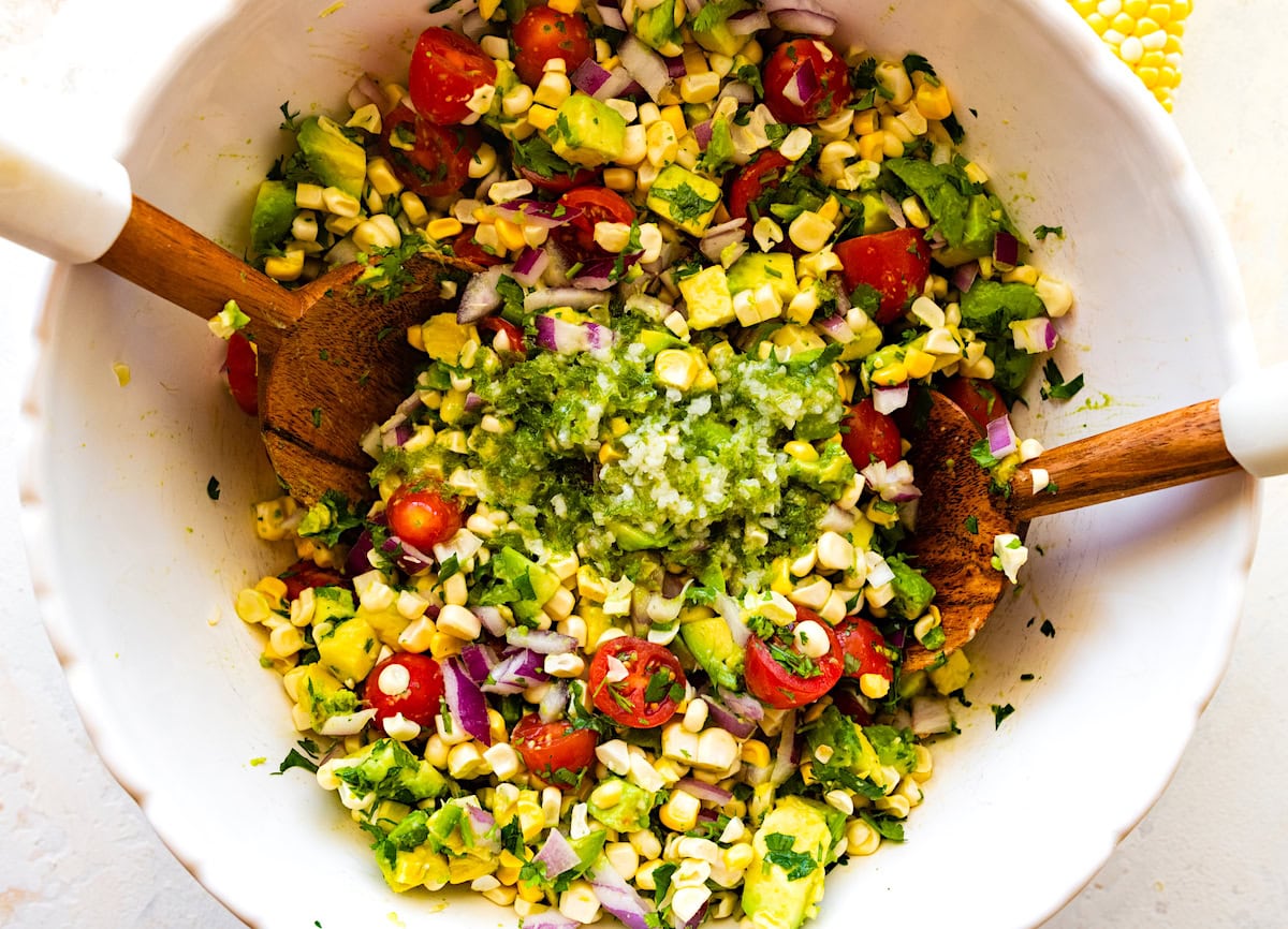 avocado corn salad in mixing bowl with salad servers.