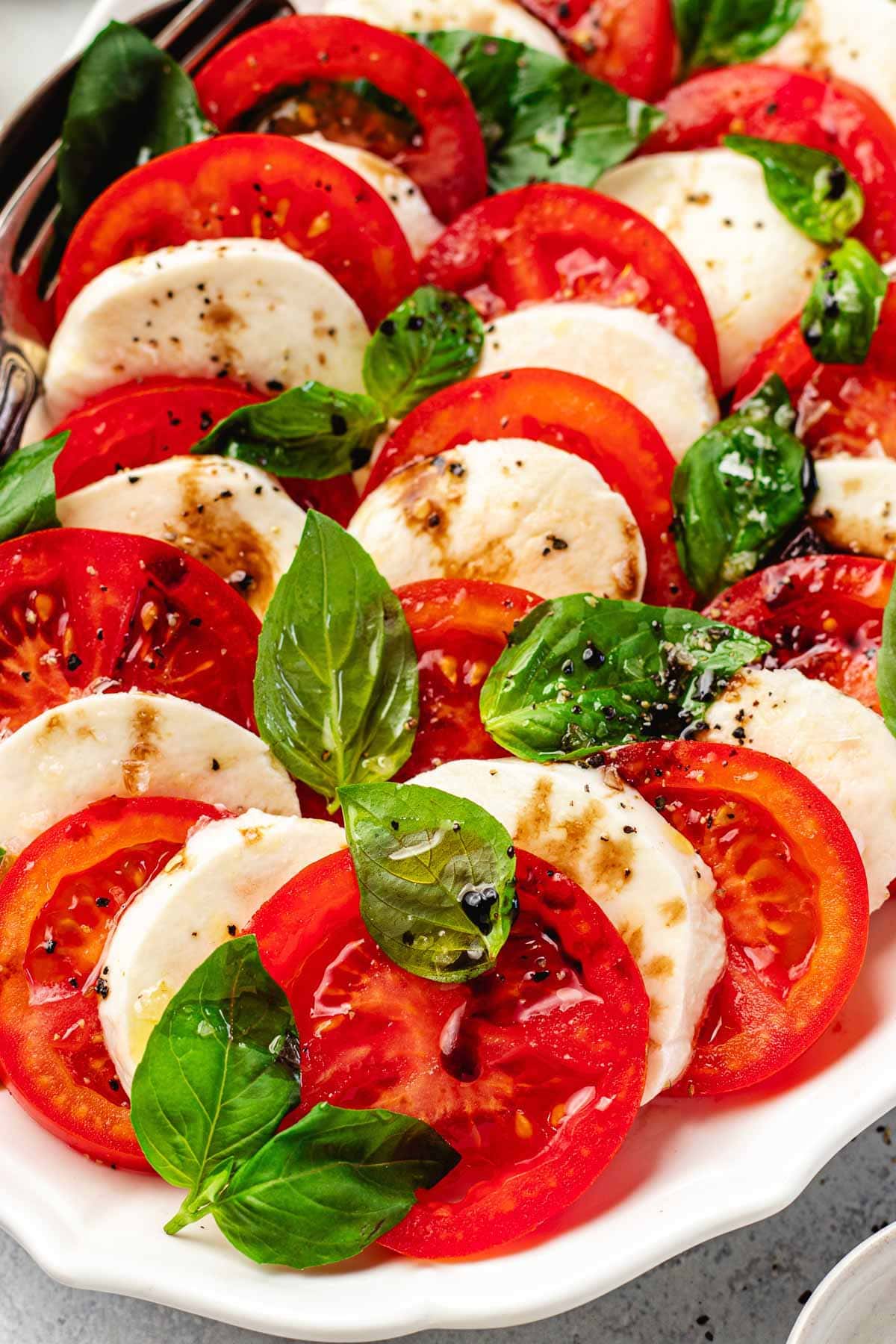 close up of caprese salad with tomato slices, fresh mozzarella slices, basil, and balsamic vinegar.