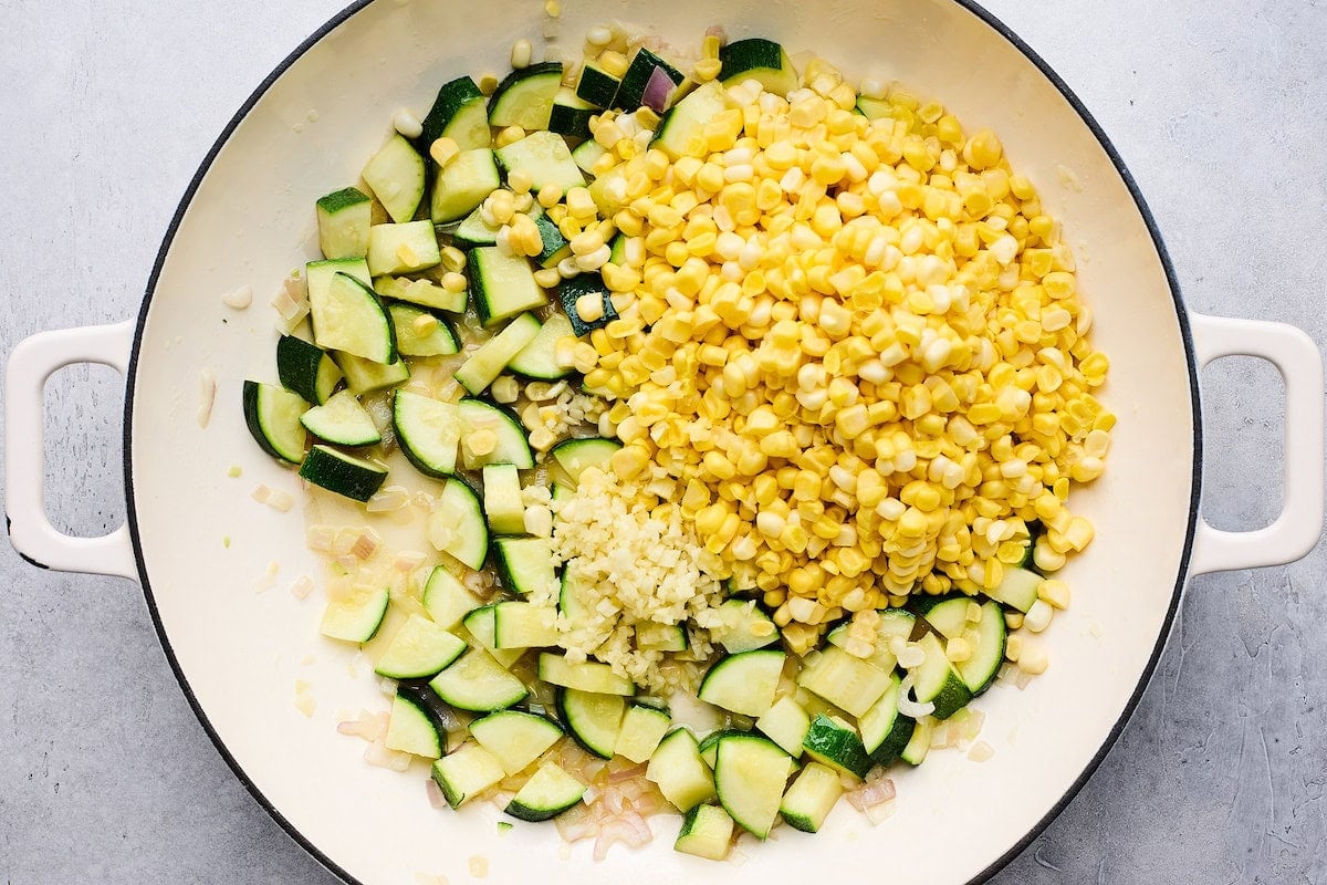 shallot, zucchini, corn, and garlic cooking in skillet.