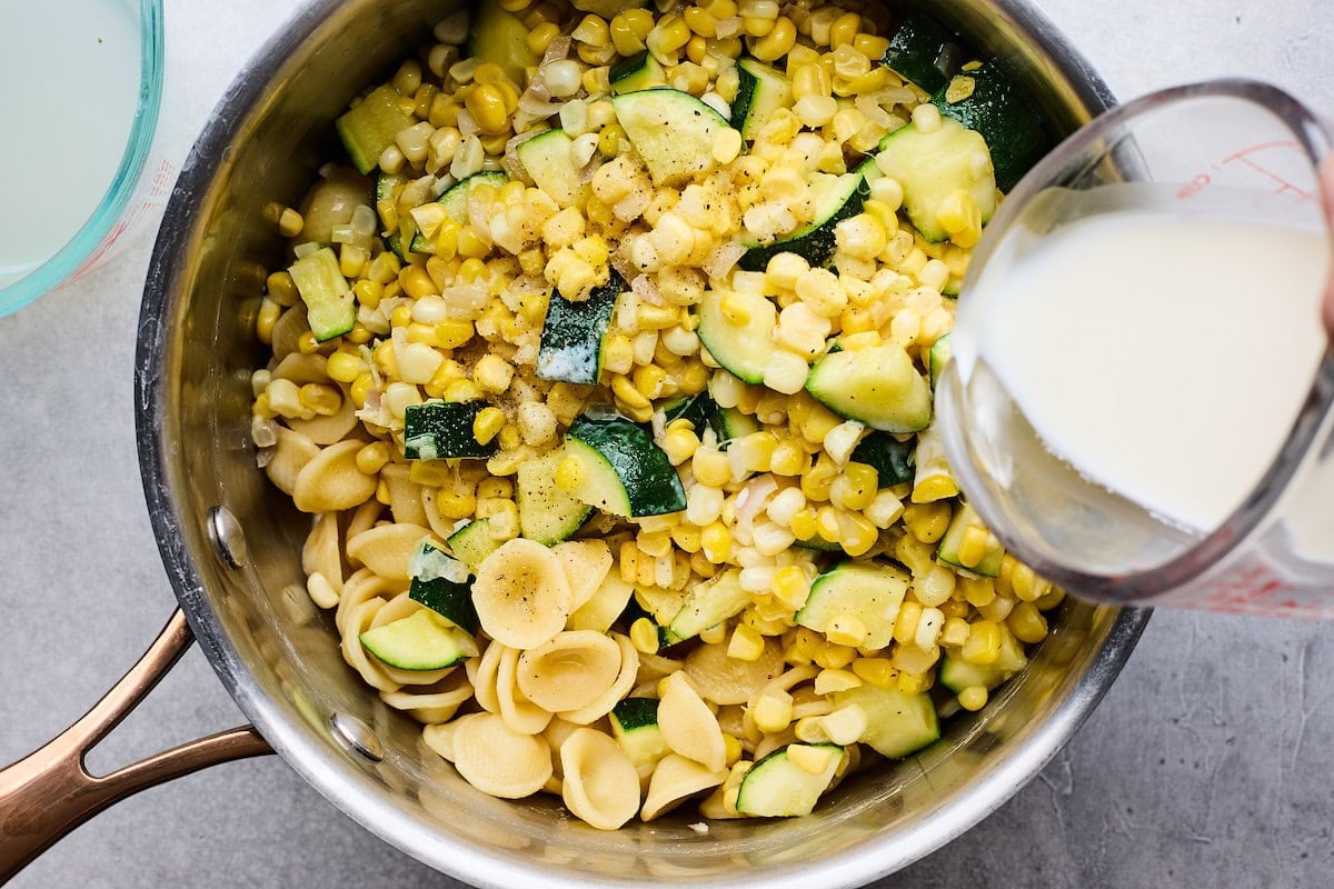 heavy cream being poured over zucchini corn pasta.