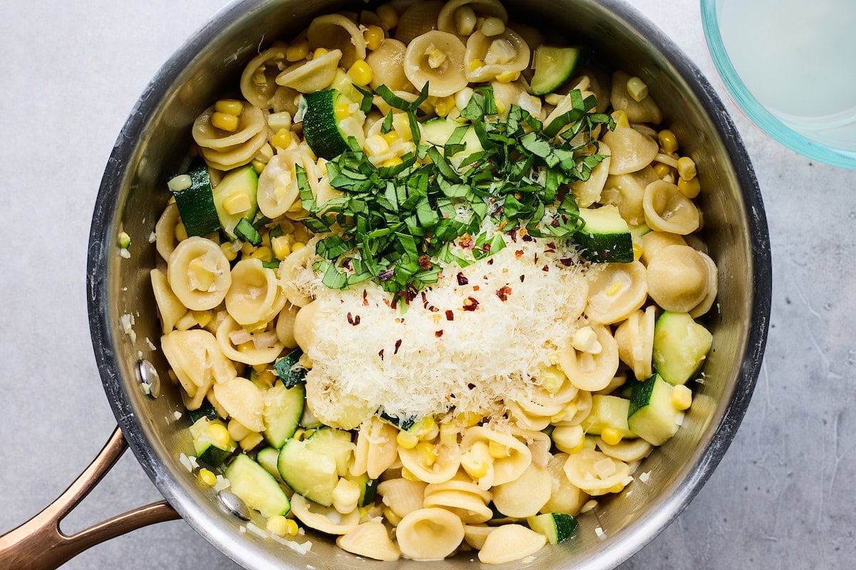 pasta, zucchini, corn, basil, parmesan cheese, and red pepper flakes in pan.