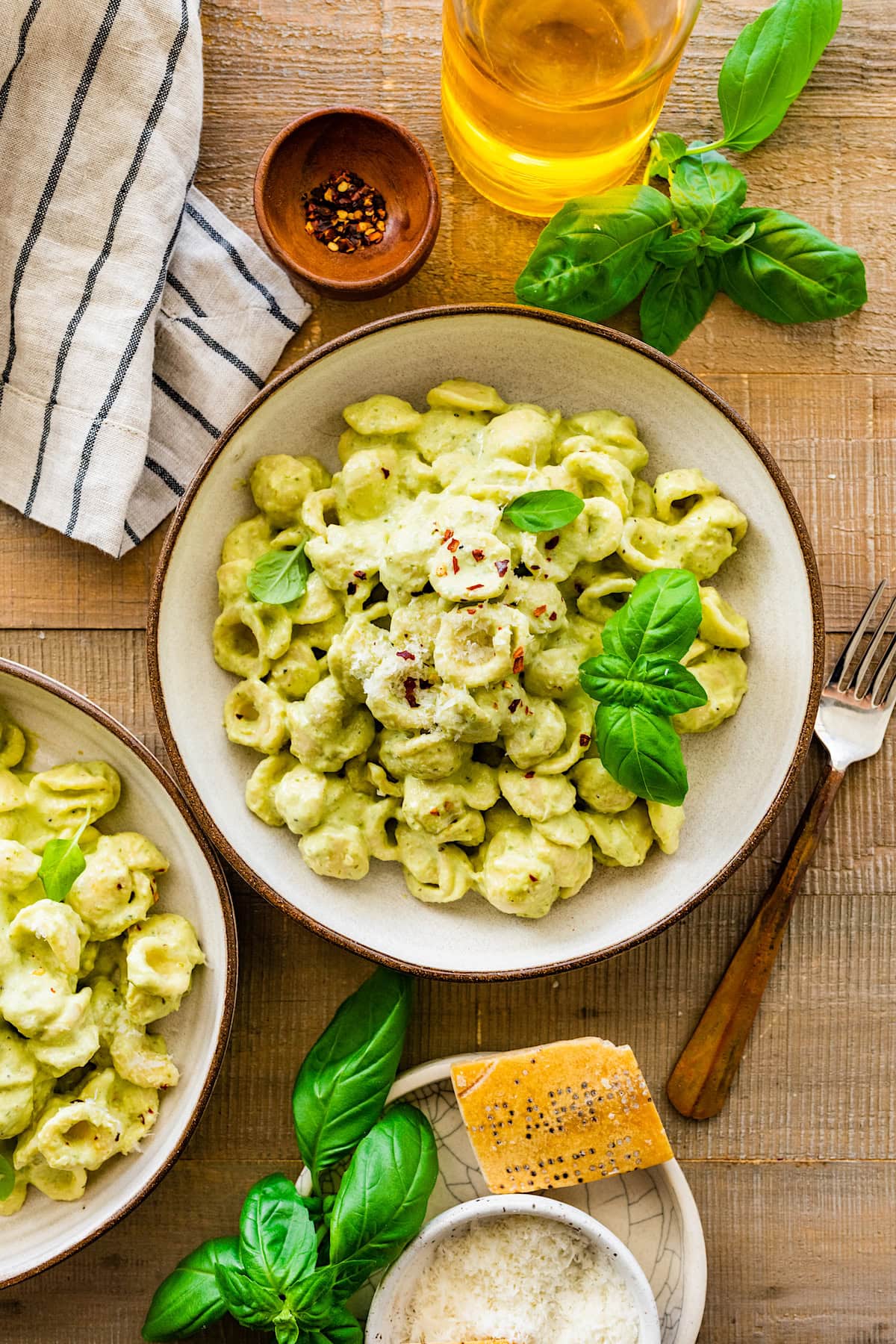 creamy pesto pasta in bowl with fresh basil, parmesan cheese, and crushed red pepper flakes.