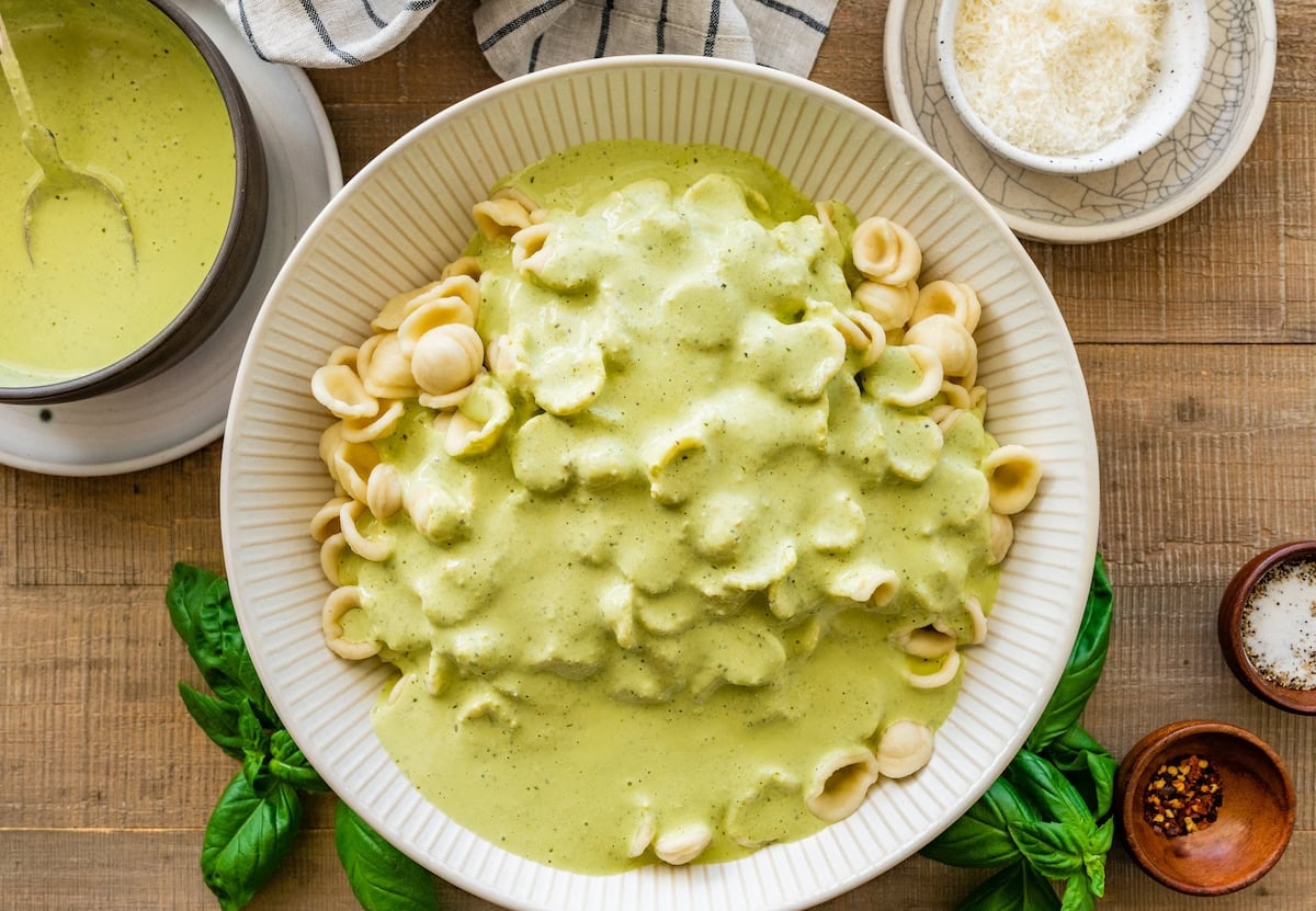creamy pesto pasta sauce poured over pasta in bowl.