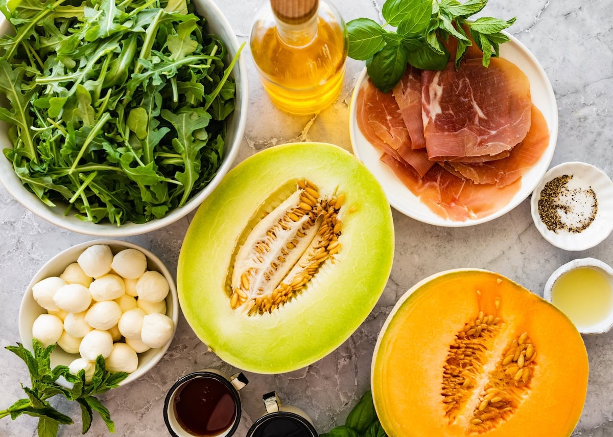 arugula, olive oil, basil, prosciutto, fresh mozzarella, and melons to make melon and prosciutto salad.
