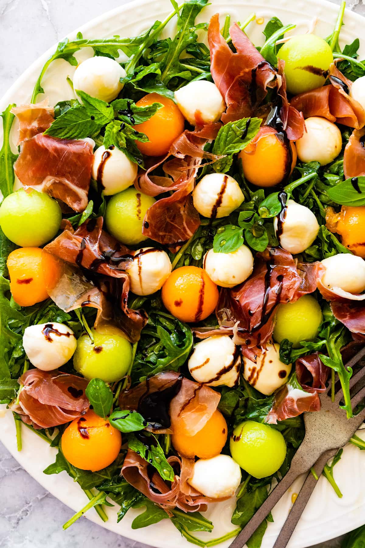 melon and prosciutto salad wit balsamic glaze on platter.