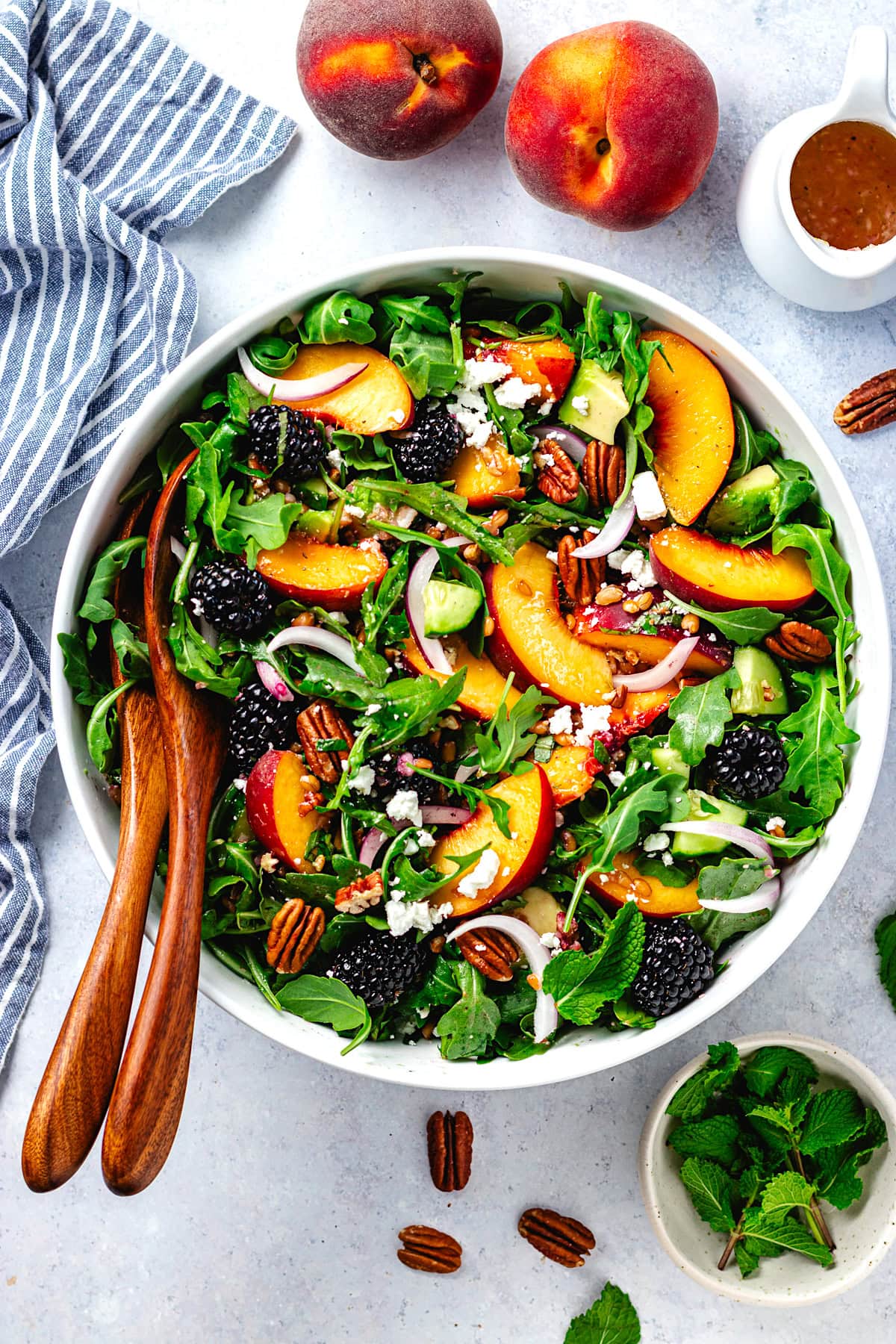 blackberry peach arugula salad with farro, pecans, red onion, feta cheese, avocado, and cucumber in bowl with wood salad servers.
