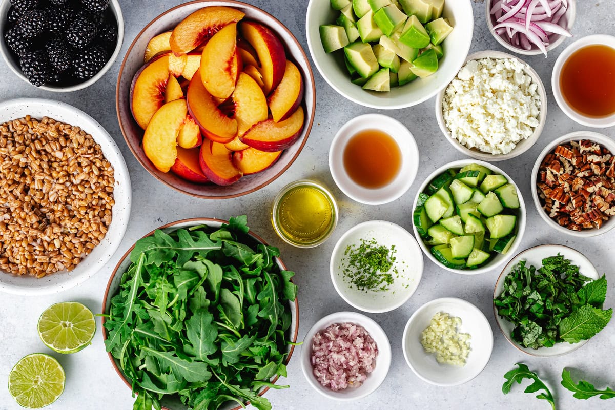 ingredients in bowls to make blackberry peach arugula salad.