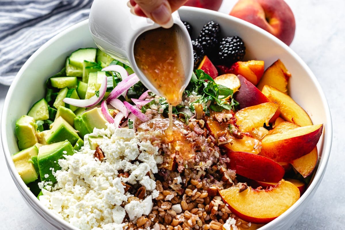 honey lime dressing being poured over blackberry peach arugula salad in bowl.
