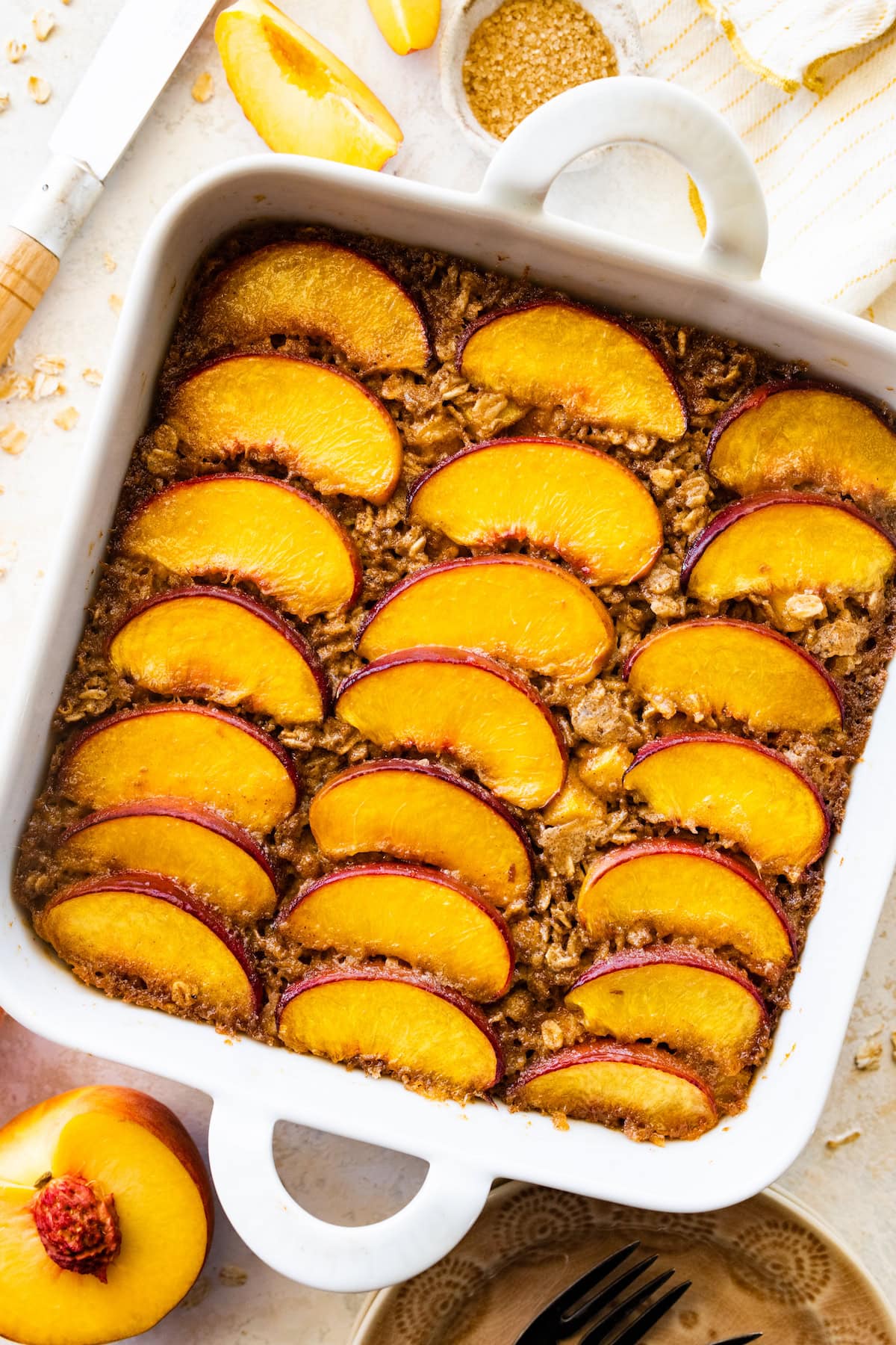 brown butter peach baked oatmeal in white pan with fresh peach slices on top.