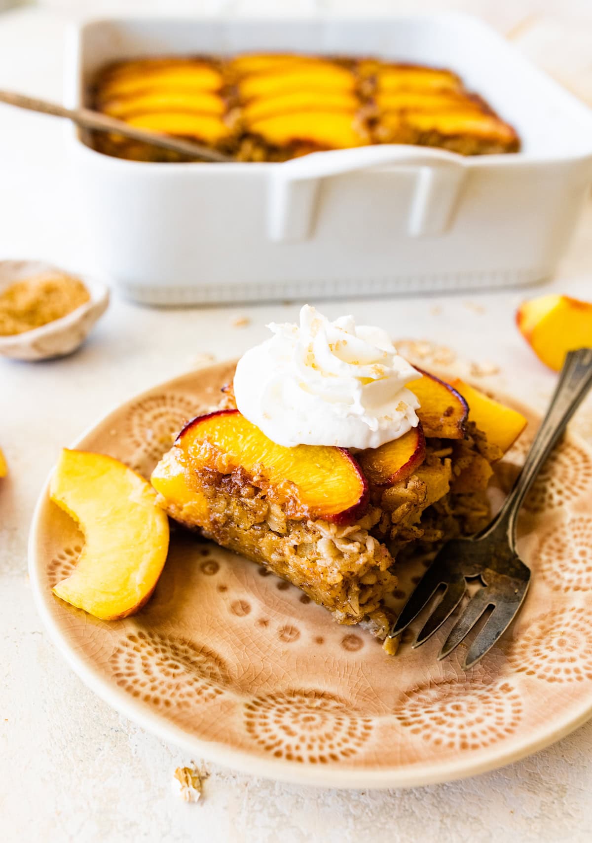 peach baked oatmeal on plate with whipped cream, fresh peach slices, and whipped cream.