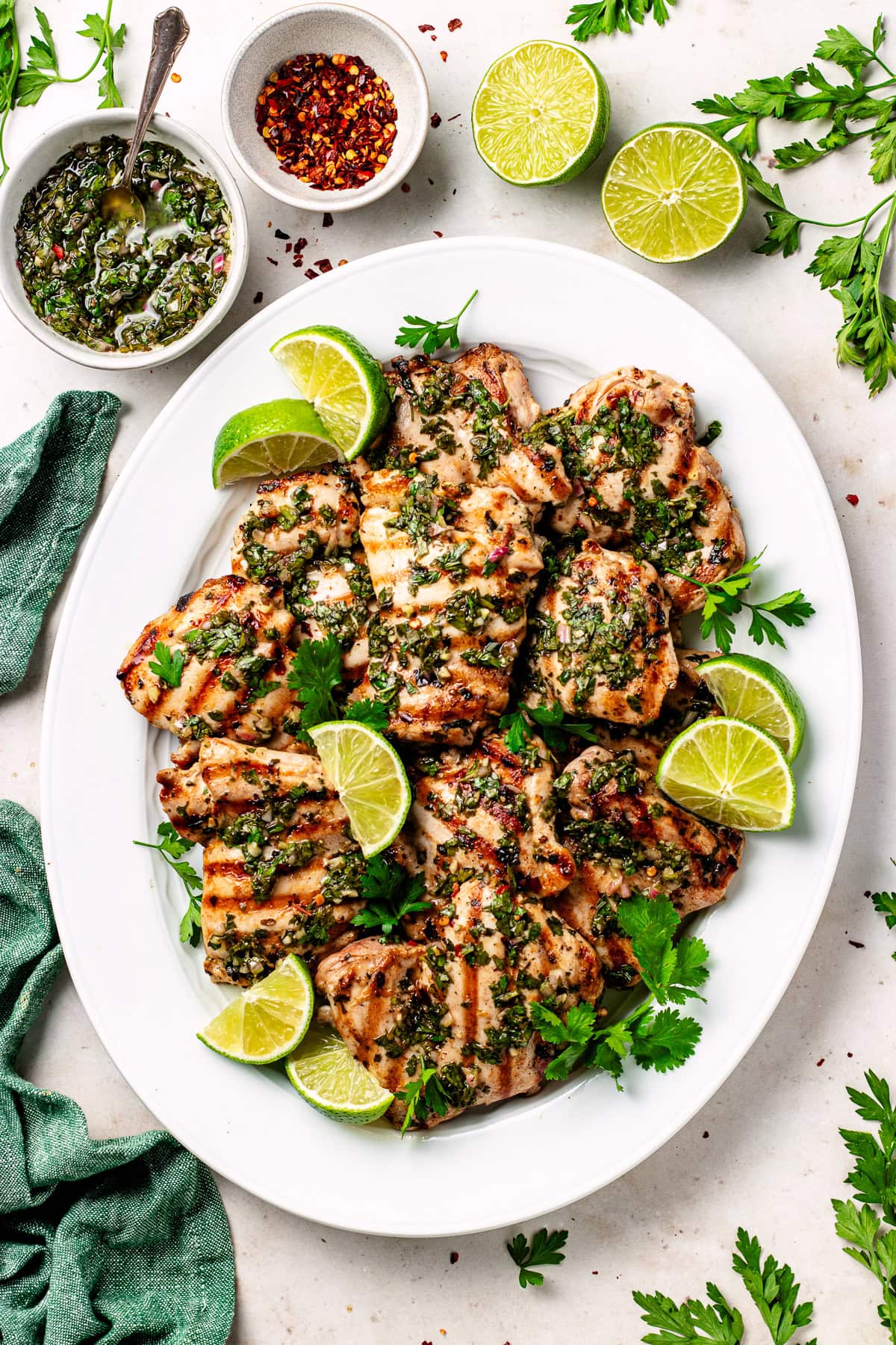 grilled chimichurri chicken on platter with lime wedges and herbs.