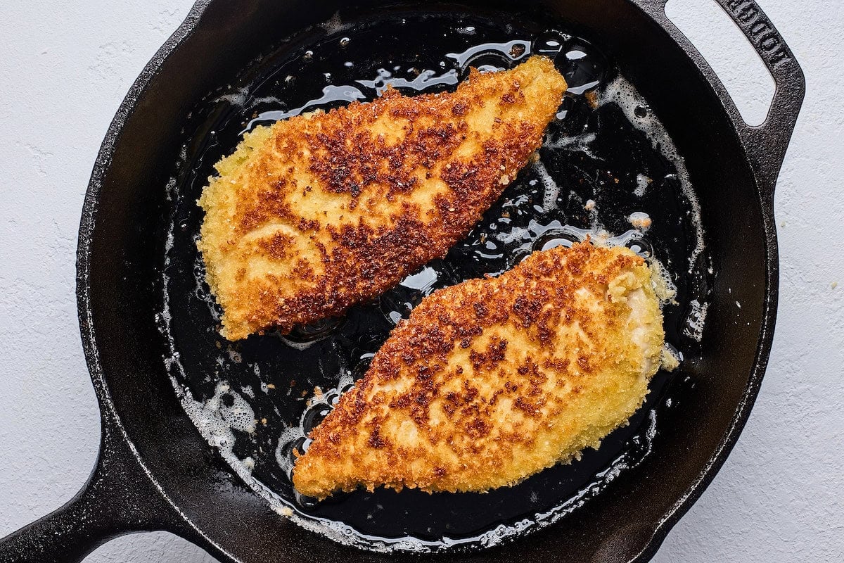 crispy chicken cooking in cast iron skillet.