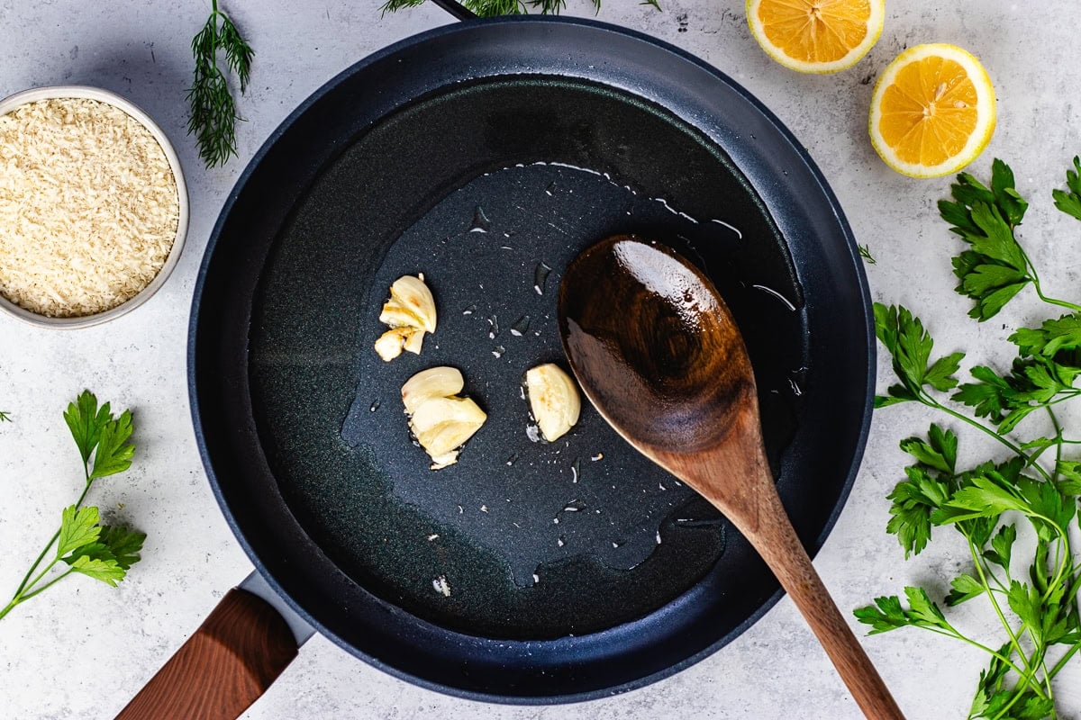 garlic cooking in olive oil in skillet with wooden spoon.