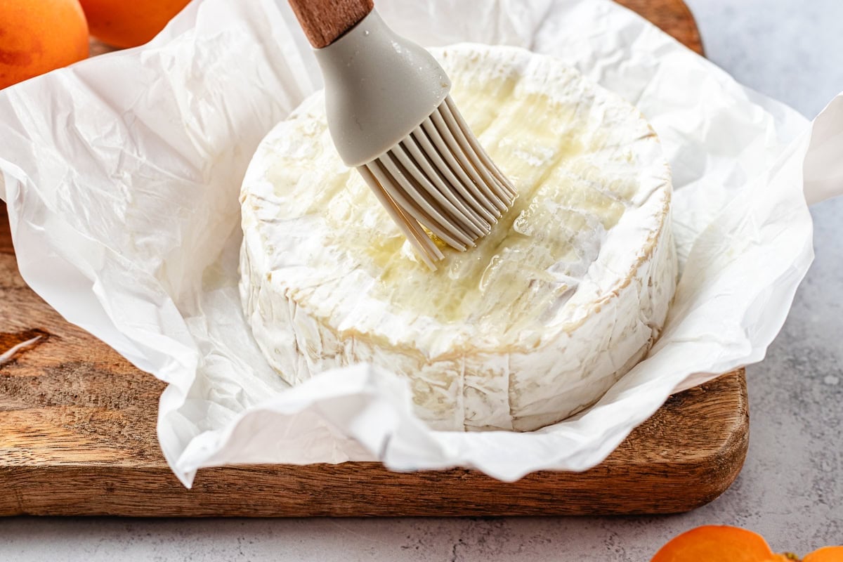 olive oil being brushed on top of a round of brie cheese.