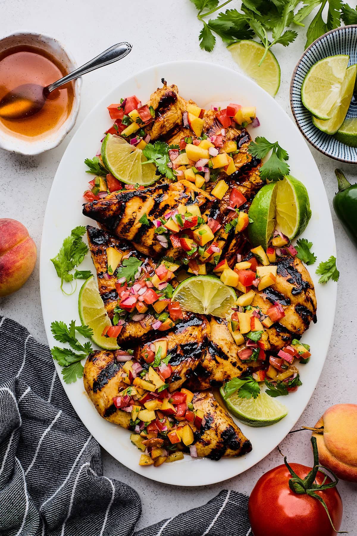 hot honey chicken on platter with peach pico de gallo, lime wedges, and cilantro.