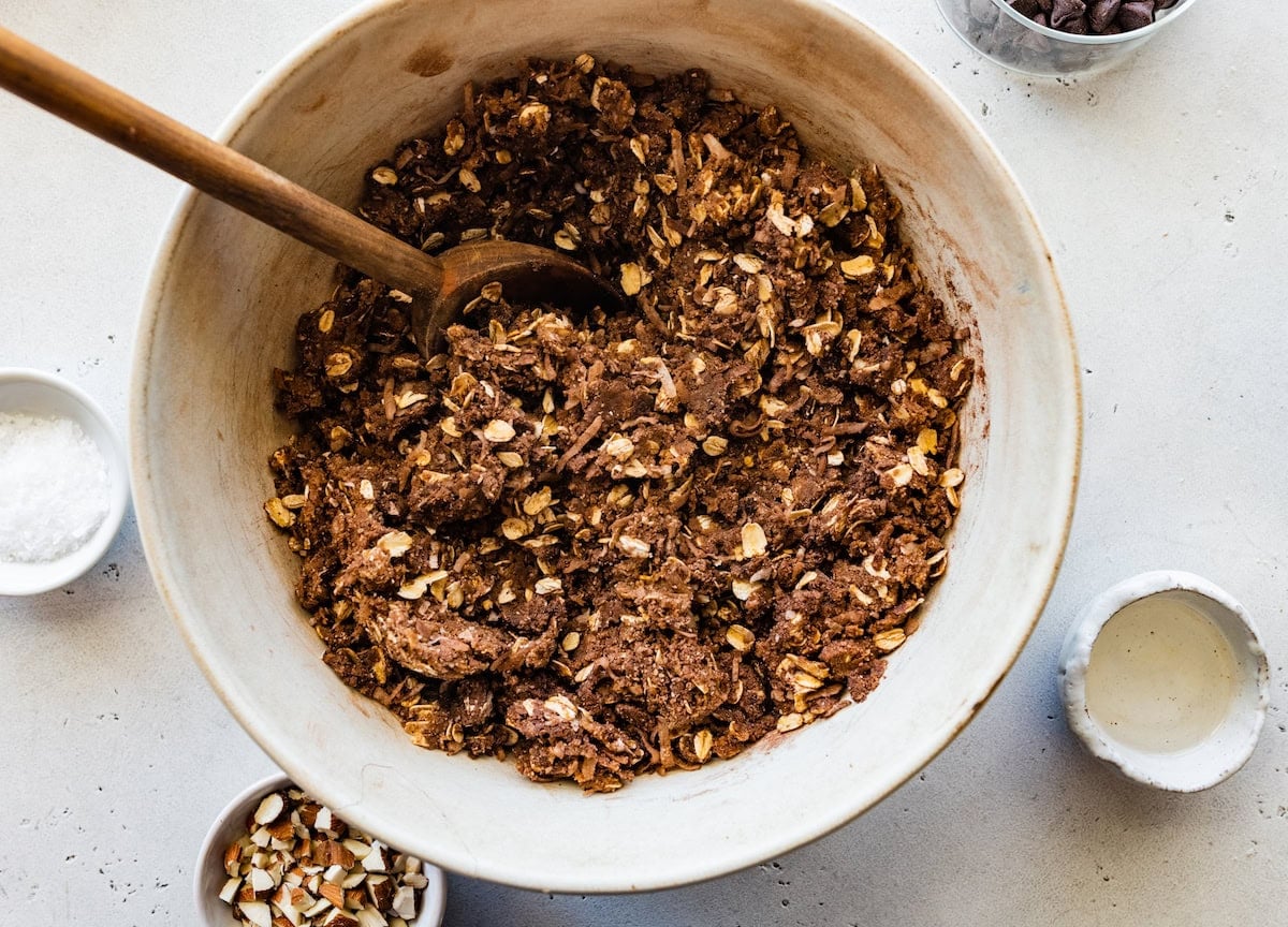 chocolate oat coconut mixture in mixing bowl with wooden spoon.