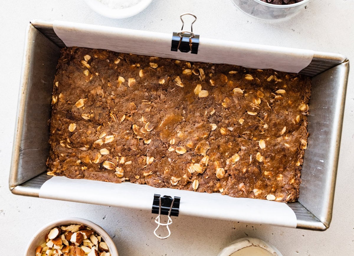 chocolate coconut oat mixture pressed in loaf pan lined with parchment paper to make no bake almond joy bars.