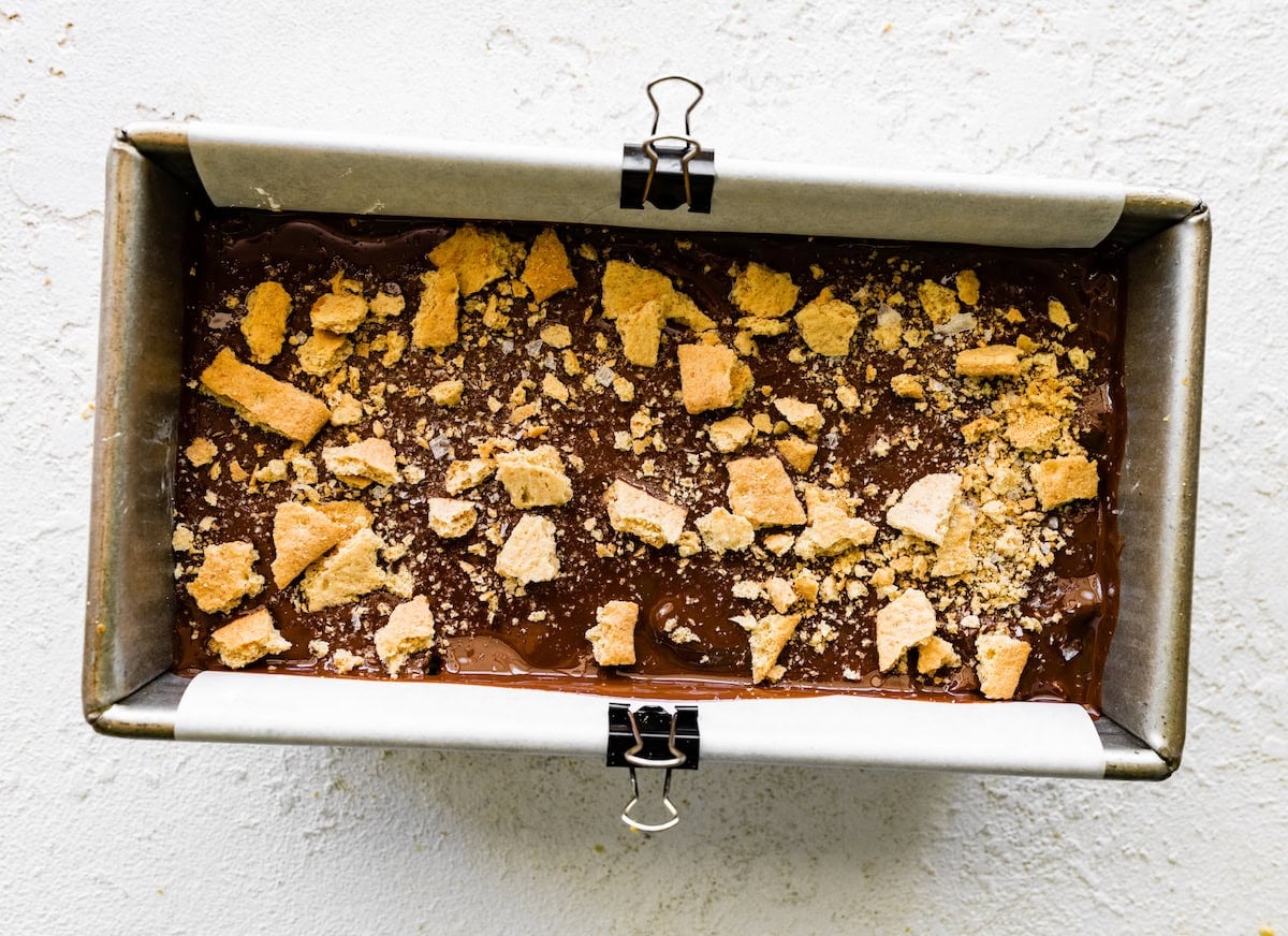 layering chocolate and graham cracker pieces in loaf pan to make no bake peanut butter s'mores bars.