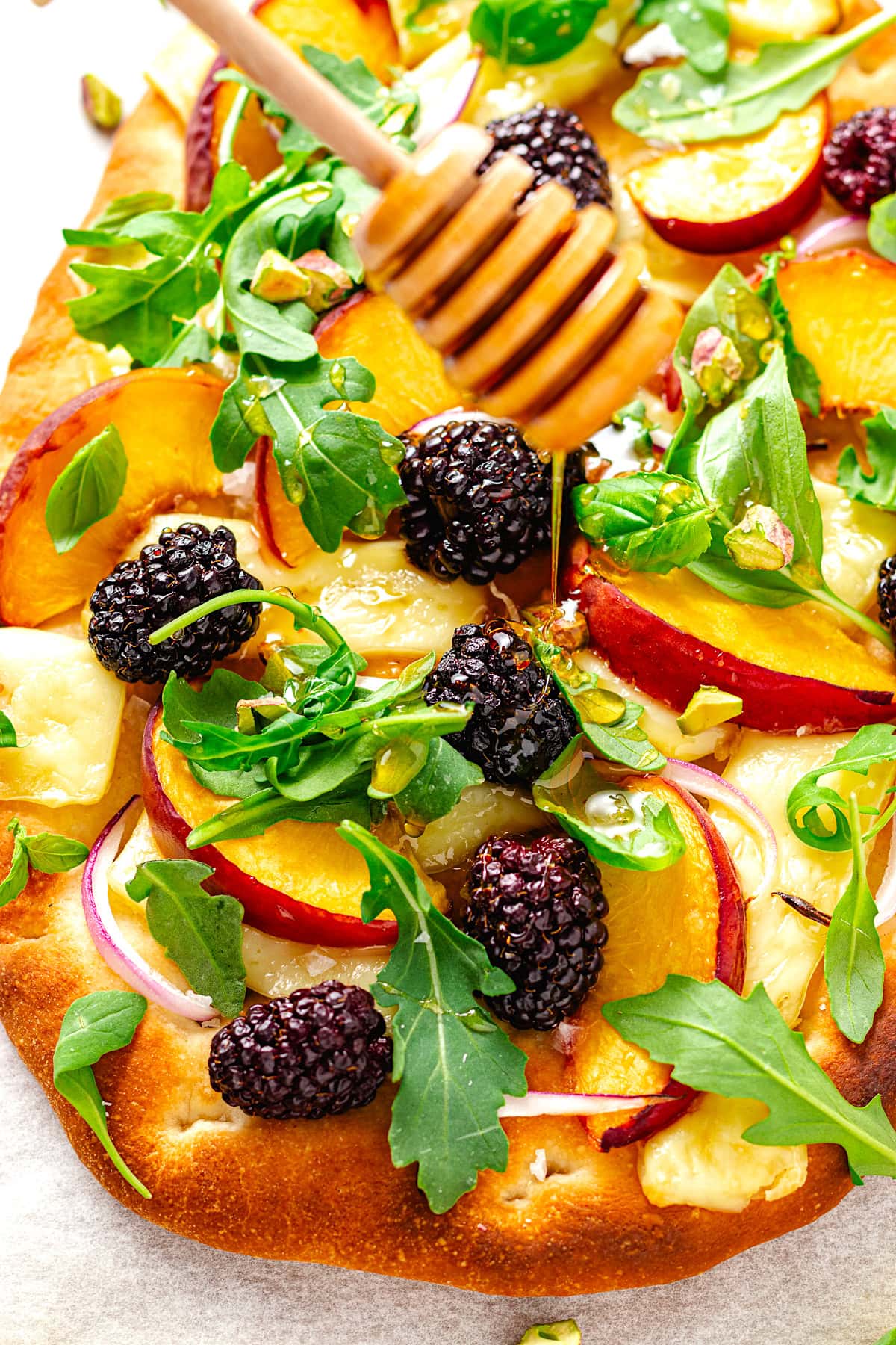 drizzling honey on peach brie flatbread with blackberries, arugula, red onion, and pistachios.