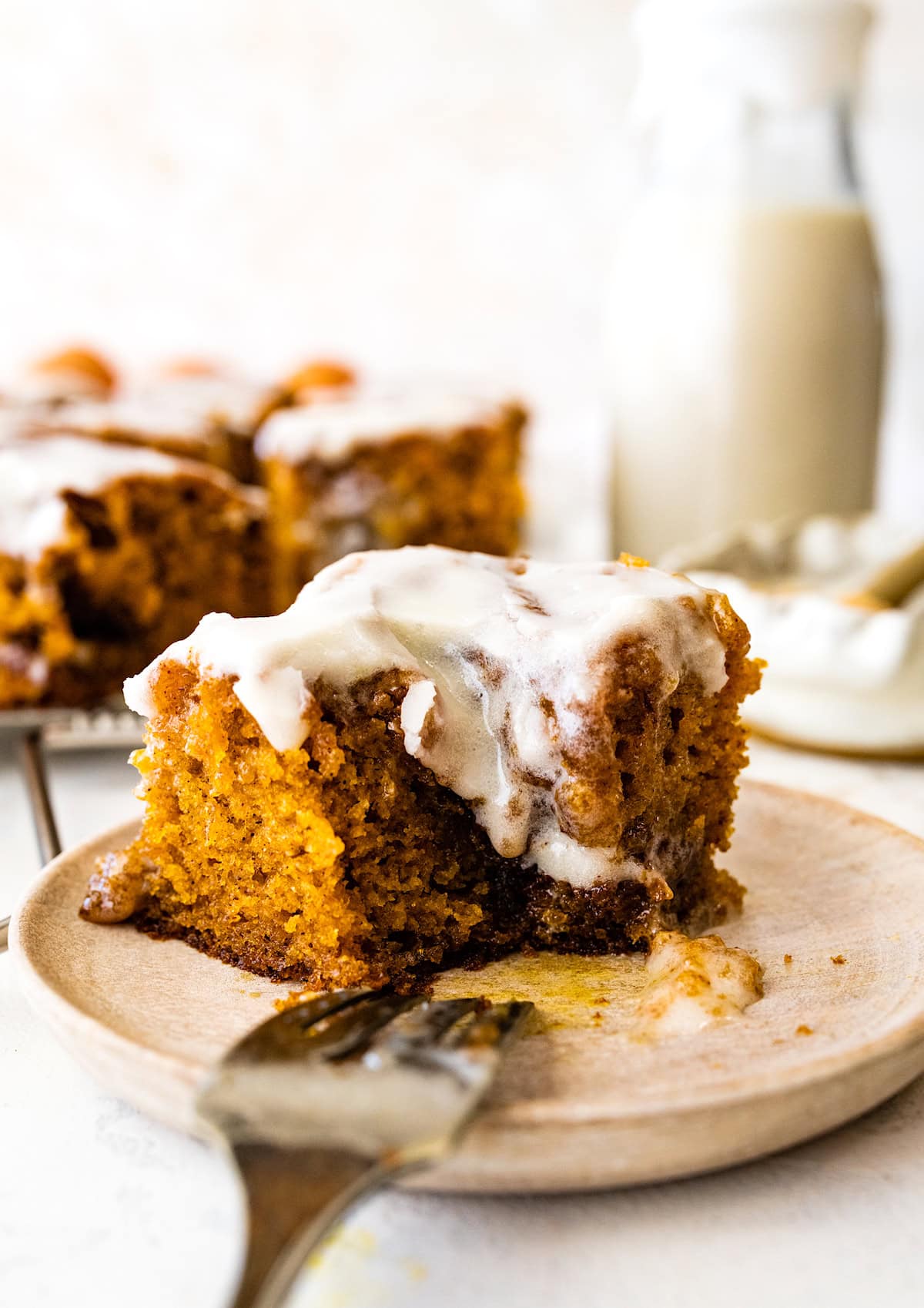 piece of cinnamon swirl pumpkin cake with cream cheese icing on plate with fork.