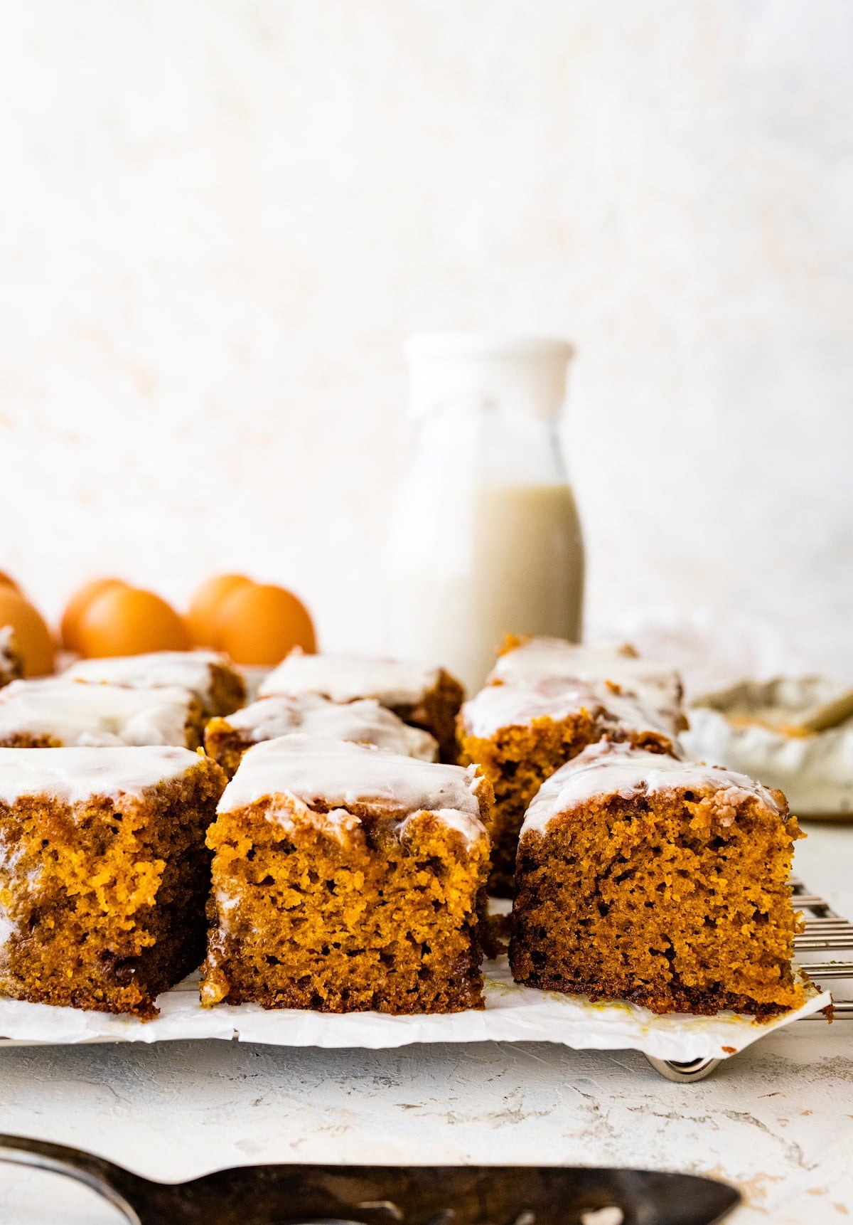 cinnamon swirl pumpkin cake cut into squares on cooling rack with bottle of milk.