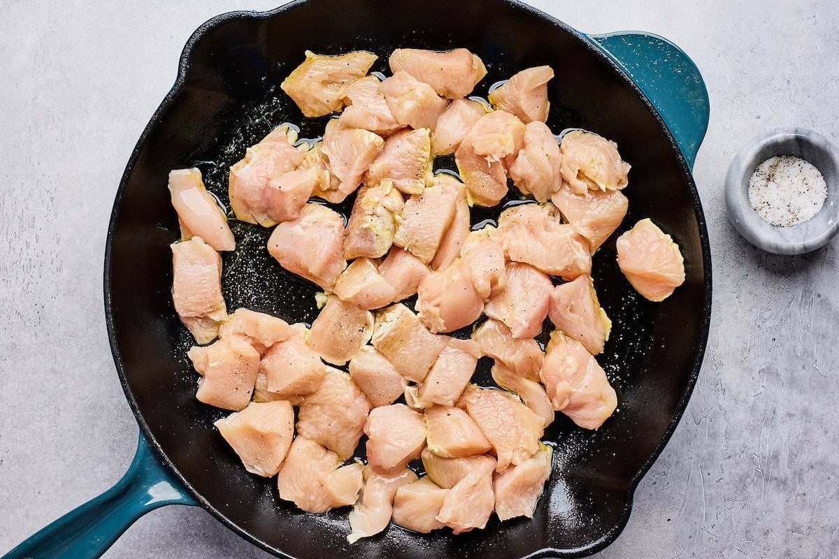 cut up chicken breasts cooking in cast iron skillet.