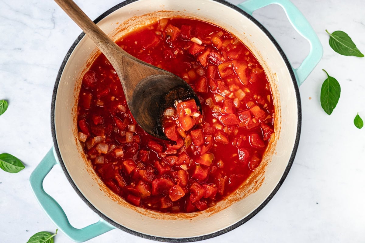 tomatoes, onion, and garlic in pot with wooden spoon to make cottage cheese pasta sauce.